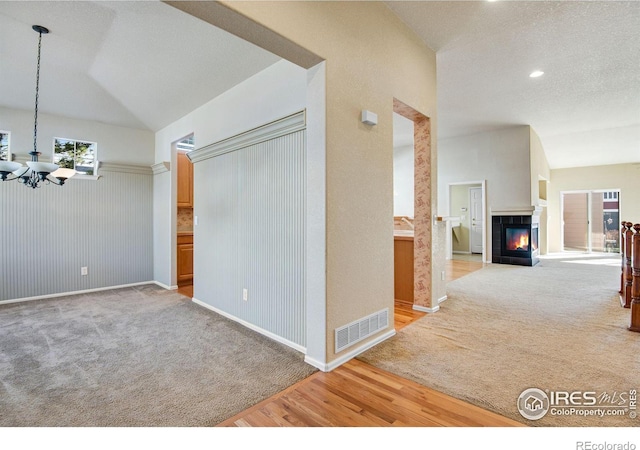 corridor featuring a chandelier, visible vents, vaulted ceiling, and light colored carpet