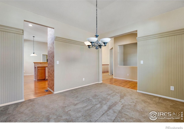 carpeted empty room featuring baseboards and an inviting chandelier