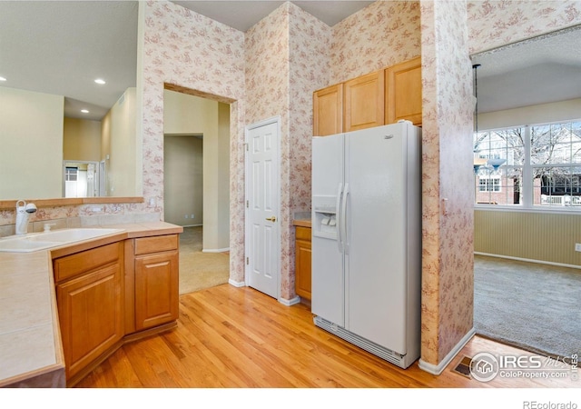 kitchen with white fridge with ice dispenser, light wood-style floors, a sink, and wallpapered walls