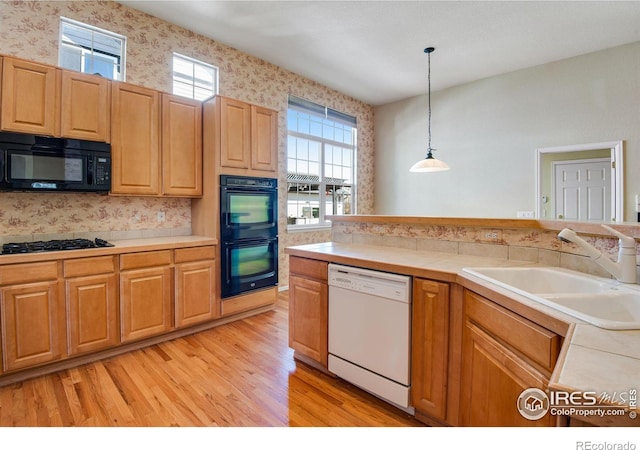 kitchen with light wood-style flooring, a sink, hanging light fixtures, black appliances, and wallpapered walls