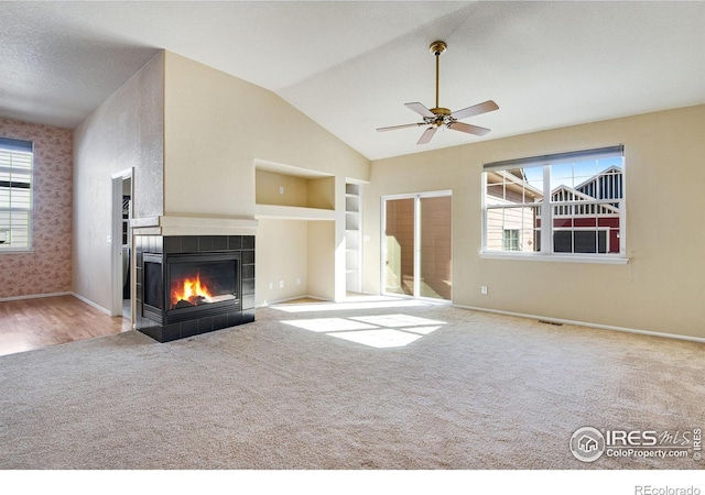 unfurnished living room with built in shelves, carpet, lofted ceiling, a tile fireplace, and baseboards