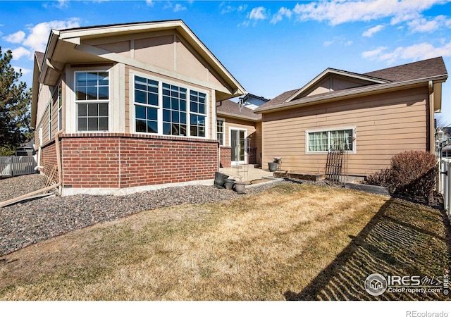 rear view of house with fence, a lawn, and brick siding