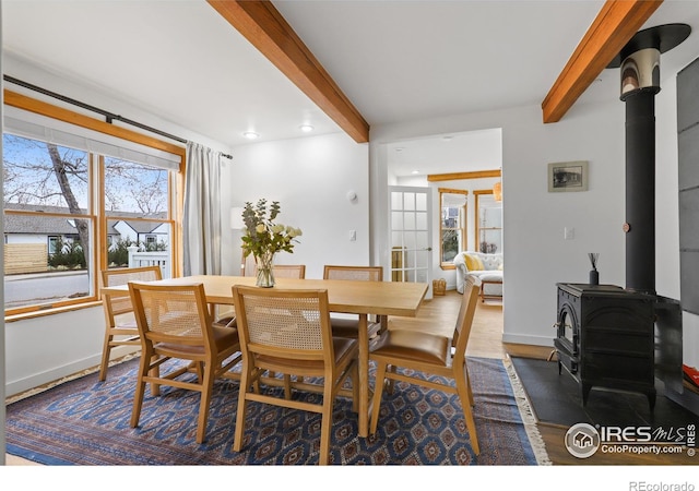 dining area with beamed ceiling, wood finished floors, a wood stove, and baseboards