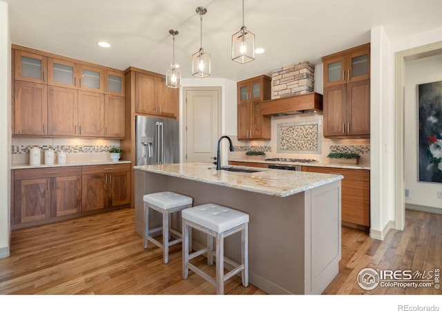 kitchen featuring stainless steel appliances, brown cabinetry, a sink, and a center island with sink