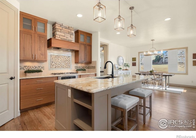 kitchen with wood finished floors, a sink, brown cabinets, tasteful backsplash, and a center island with sink