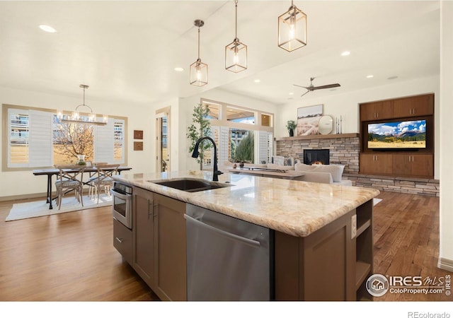 kitchen featuring stainless steel appliances, a fireplace, wood finished floors, a sink, and a center island with sink