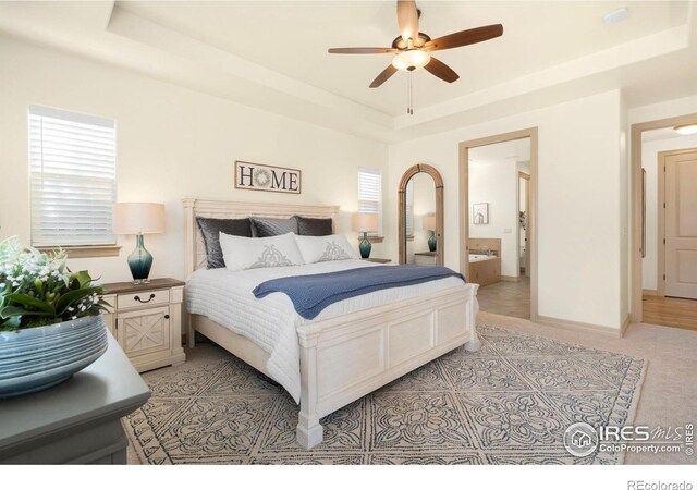 bedroom featuring a ceiling fan, baseboards, a raised ceiling, and connected bathroom