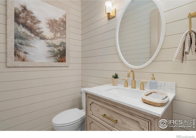 half bath featuring toilet, wood walls, and vanity