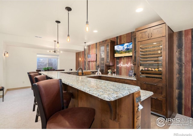 kitchen with light stone counters, hanging light fixtures, glass insert cabinets, light carpet, and a kitchen breakfast bar