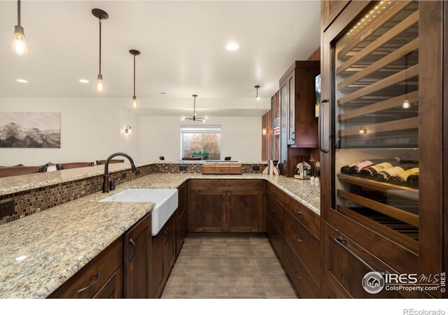 kitchen featuring decorative light fixtures, a sink, dark brown cabinetry, light stone countertops, and beverage cooler