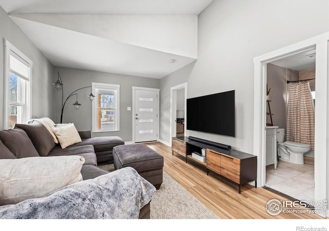 living area featuring vaulted ceiling, light wood-style flooring, and baseboards