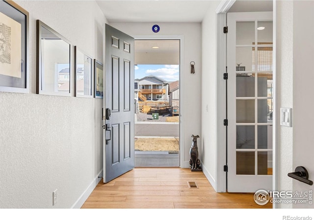 doorway with light wood-style floors, baseboards, visible vents, and a textured wall