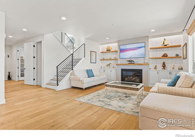 living area with recessed lighting, baseboards, stairway, light wood finished floors, and a glass covered fireplace