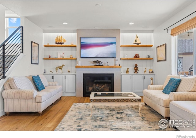 living room featuring a large fireplace, light wood-style flooring, stairway, and recessed lighting