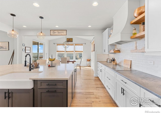 kitchen with decorative backsplash, black electric stovetop, custom exhaust hood, open shelves, and a sink