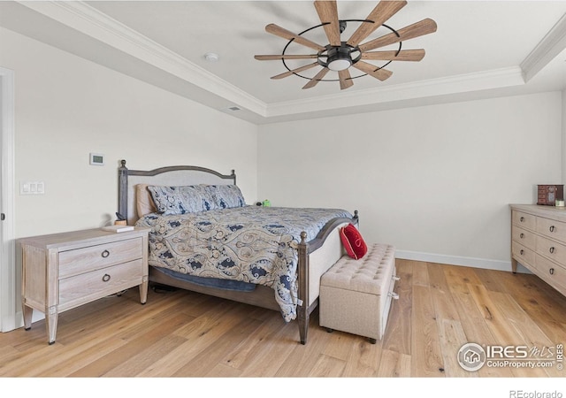 bedroom with ornamental molding, a tray ceiling, baseboards, and light wood finished floors