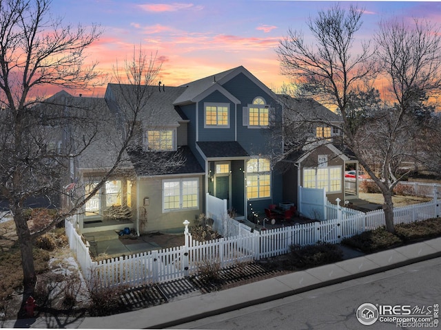 traditional home with a fenced front yard, a gate, and roof with shingles