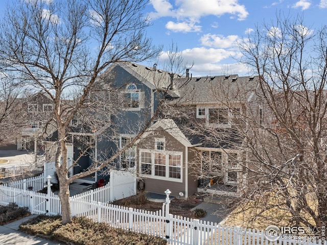 back of house featuring a shingled roof, a fenced front yard, and a gate