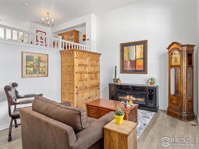 living room featuring a glass covered fireplace, a notable chandelier, light wood-style flooring, and baseboards