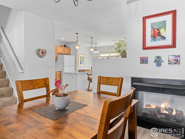 dining room with light wood-style flooring, stairway, a multi sided fireplace, and a textured ceiling