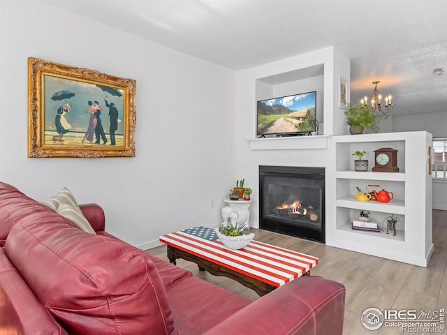 living area featuring built in shelves, a glass covered fireplace, a textured ceiling, wood finished floors, and a chandelier