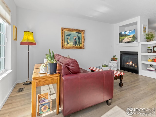 living area with built in features, visible vents, wood finished floors, and a glass covered fireplace