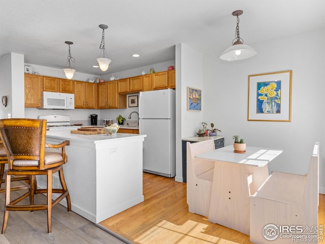 kitchen with white appliances, light wood-style flooring, a breakfast bar, decorative light fixtures, and light countertops