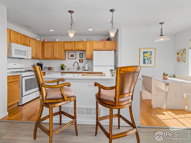 kitchen featuring light wood-type flooring, white appliances, light countertops, and decorative light fixtures