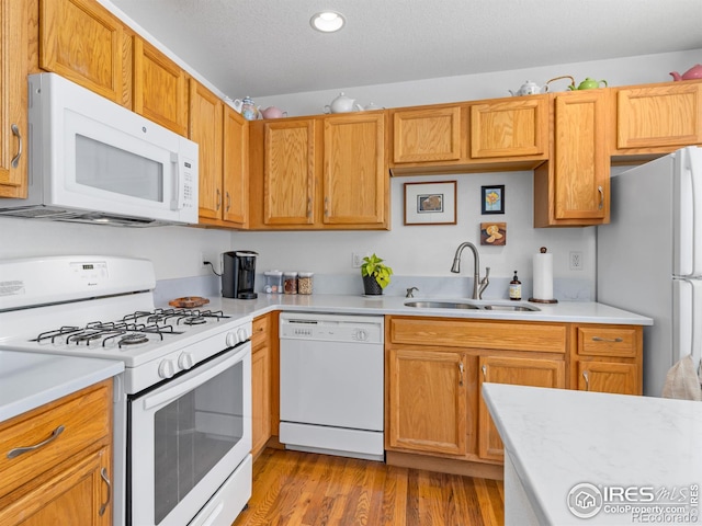 kitchen featuring white appliances, light countertops, a textured ceiling, light wood-type flooring, and a sink