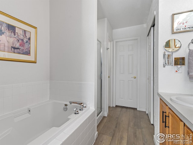 full bath featuring a bath, a shower stall, wood finished floors, and vanity