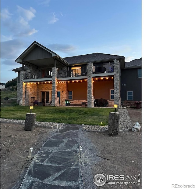 back of house with a yard, stone siding, and a balcony