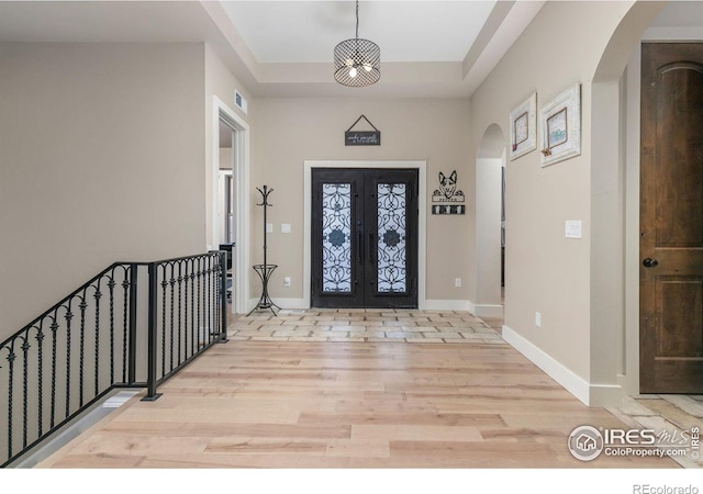 entrance foyer with light wood-style floors, baseboards, a raised ceiling, french doors, and arched walkways