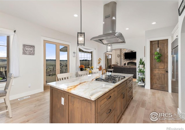 kitchen with stainless steel gas stovetop, a healthy amount of sunlight, light wood-style floors, and island range hood