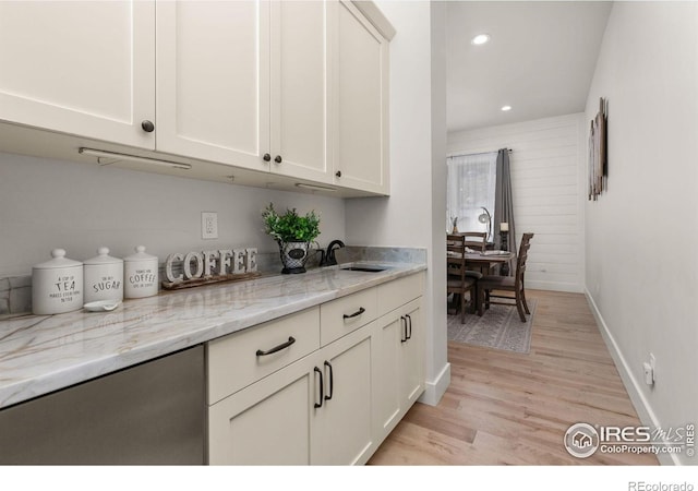 kitchen with light stone countertops, recessed lighting, white cabinetry, a sink, and light wood finished floors