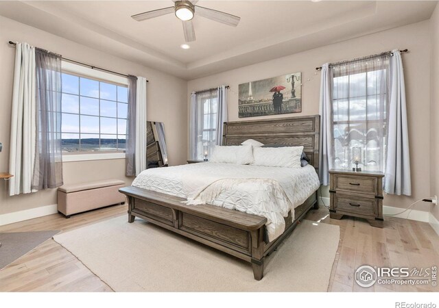 bedroom with light wood-style floors, recessed lighting, a raised ceiling, and baseboards