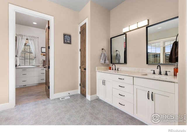 bathroom featuring a sink, baseboards, double vanity, and visible vents