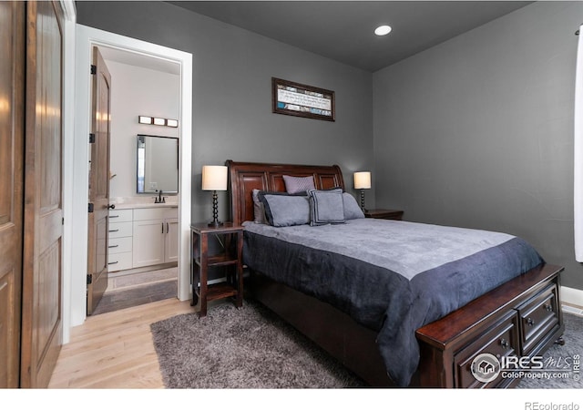 bedroom with baseboards, light wood-type flooring, recessed lighting, connected bathroom, and a sink