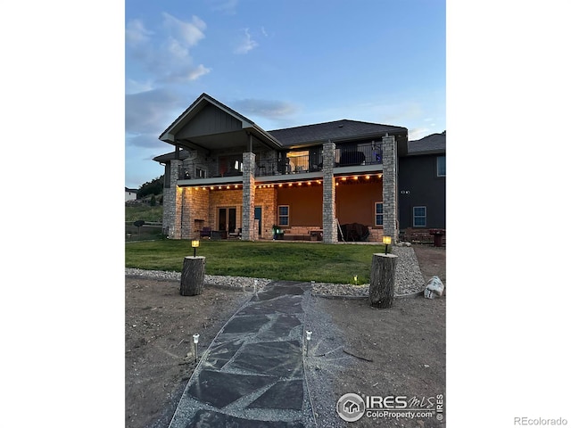 view of front facade featuring stone siding, a front yard, and a balcony