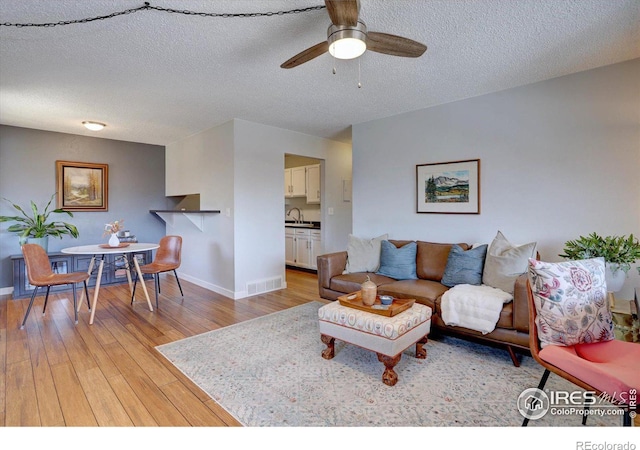 living area with light wood finished floors, visible vents, baseboards, ceiling fan, and a textured ceiling