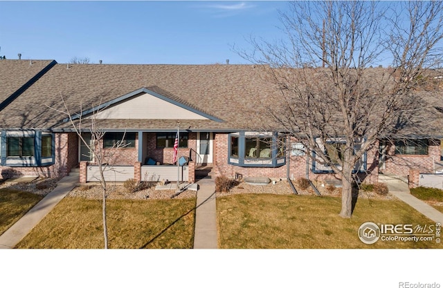 view of front of home with a shingled roof, covered porch, brick siding, and a front lawn