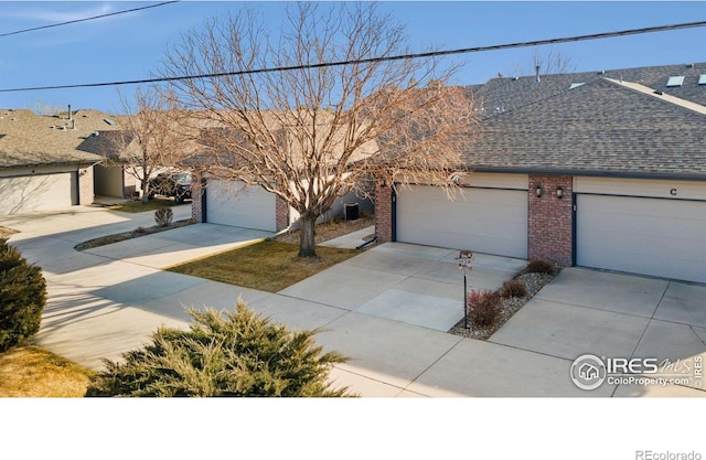 view of front of home featuring driveway, brick siding, and roof with shingles