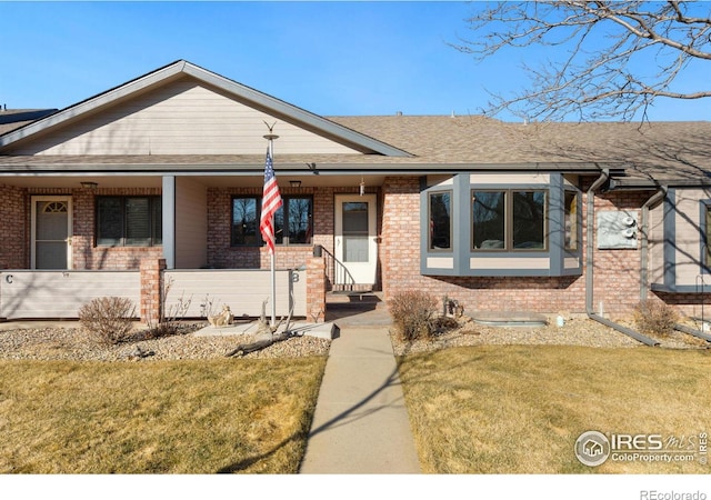 view of front of house with a porch, brick siding, a front lawn, and roof with shingles