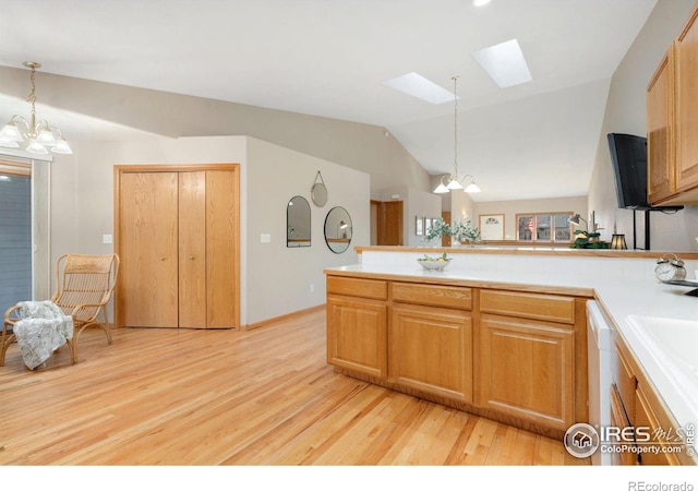 kitchen featuring a chandelier, a peninsula, vaulted ceiling with skylight, and light countertops