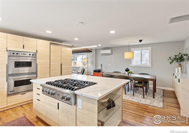 kitchen with visible vents, light wood-style flooring, a wall mounted air conditioner, stainless steel appliances, and light brown cabinets