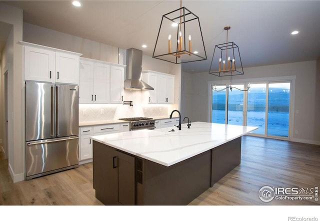 kitchen featuring a spacious island, a sink, white cabinetry, wall chimney range hood, and high end appliances