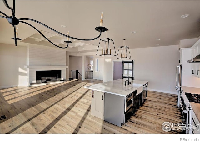 kitchen with an island with sink, light wood-style flooring, white cabinetry, and hanging light fixtures