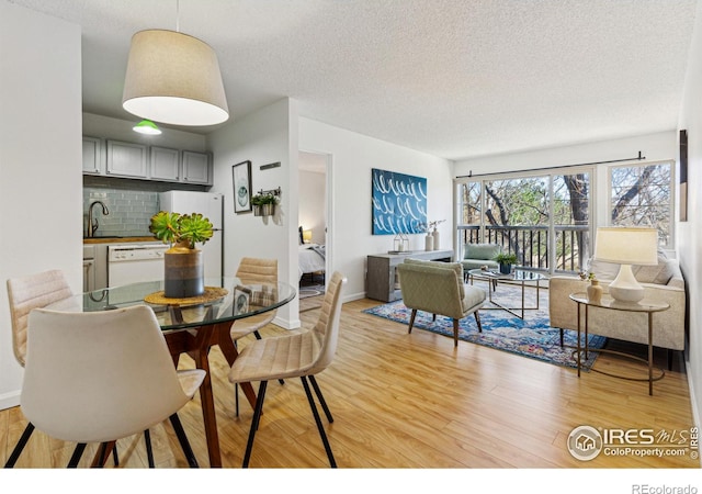 dining space with a textured ceiling, baseboards, and light wood-style floors