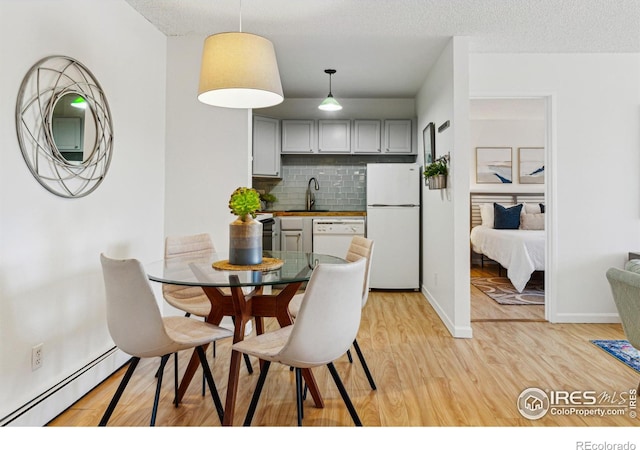 dining space with light wood-style floors, baseboards, a textured ceiling, and baseboard heating