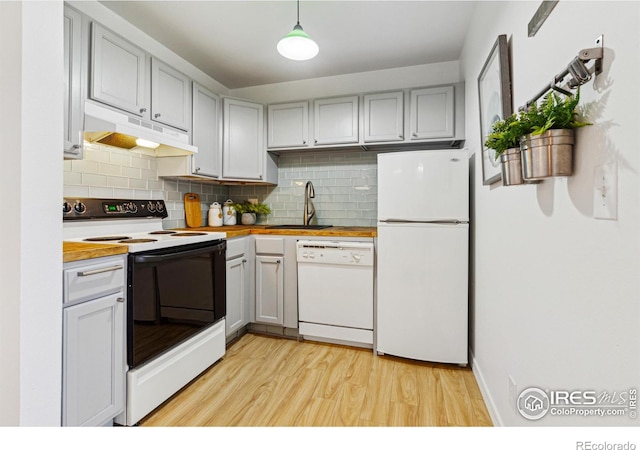 kitchen with white appliances, tasteful backsplash, light wood-style floors, under cabinet range hood, and a sink