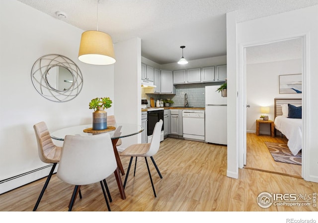 kitchen featuring white appliances, a baseboard radiator, light wood-style flooring, under cabinet range hood, and backsplash